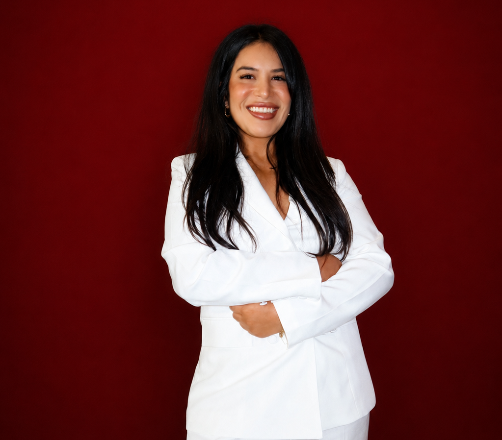 Smiling person in a white suit with arms crossed against a dark red background
