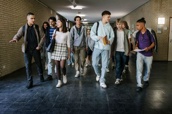 Sei studenti camminano insieme in un corridoio, chiacchierando e portando zaini e libri.
