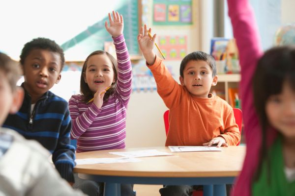Studenti che alzano la mano in classe, seduti ai banchi con magliette colorate