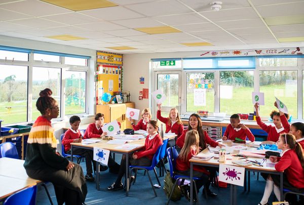 Un'insegnante conduce un'attività in classe con bambini seduti ai tavoli in una stanza luminosa.