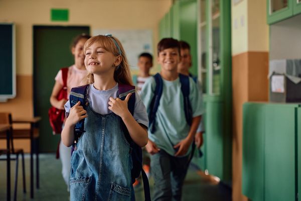 Studenti sorridenti con gli zaini in spalla che percorrono un corridoio della scuola.