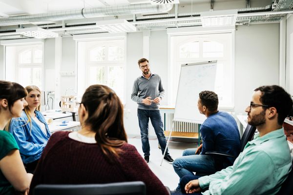 Persone sedute in una luminosa sala riunioni ascoltano un uomo in piedi che parla vicino alla finestra.