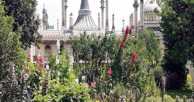 Giardino con arbusti e alberi fioriti di fronte a un sontuoso palazzo bianco.