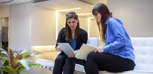 Due donne che esaminano insieme dei documenti su un divano in una moderna sala relax di un ufficio.