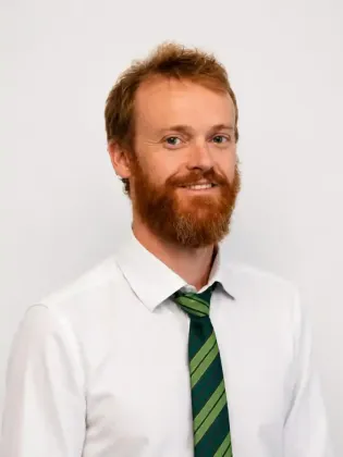 Uomo con camicia bianca e cravatta a righe verdi sorridente su uno sfondo chiaro e uniforme.
