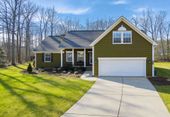 A green suburban home with a white garage door, driveway, and front porch, set against a backdrop of bare winter trees.