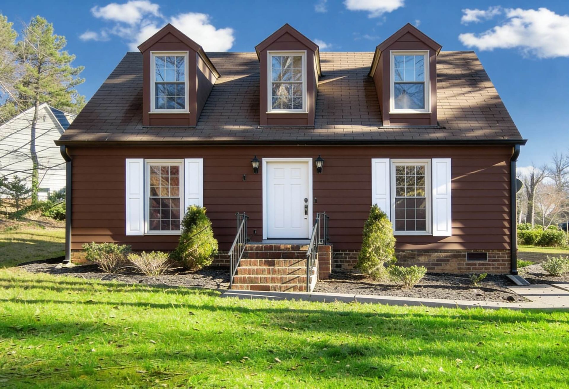 Brown house with white trim, three dormers, front steps, and green lawn.