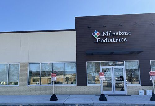 Milestone Pediatrics building with windows, a sign, and reserved parking signs on a sunny day.