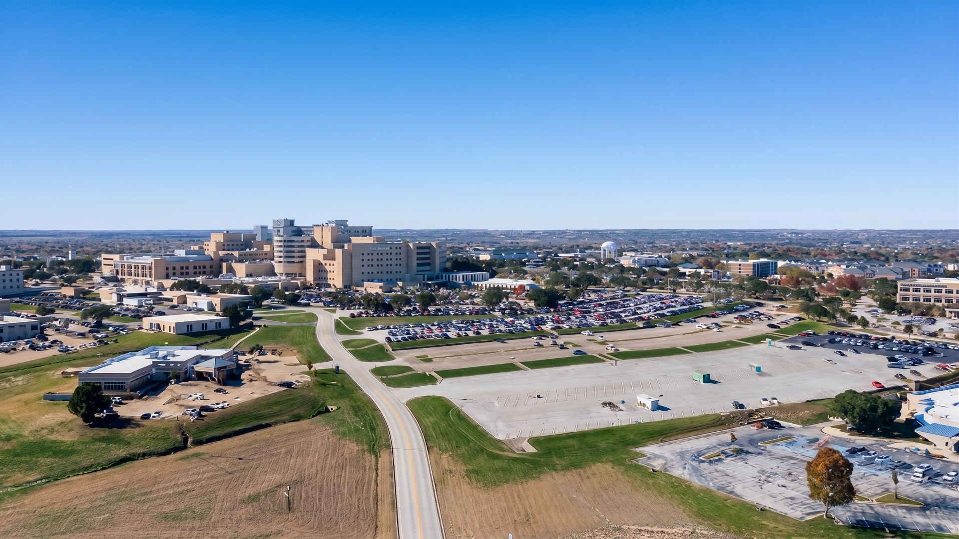 Aerial view of a developing city with roads, buildings, and open lots under a clear blue sky