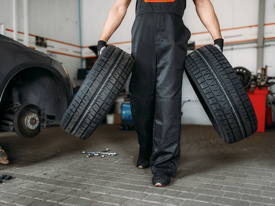 A man is holding two tires in his hands in a garage.