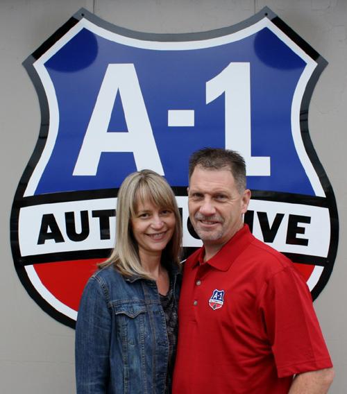A man and woman pose in front of a sign that says a-1 automotive