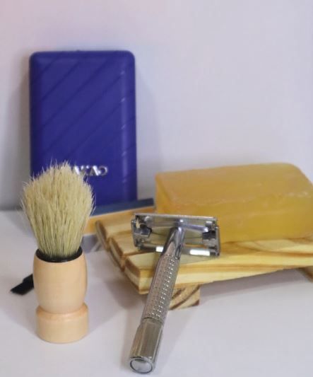 Kit de afeitado azul y amarillo con brocha y maquinilla de afeitar de seguridad sobre una superficie de madera.