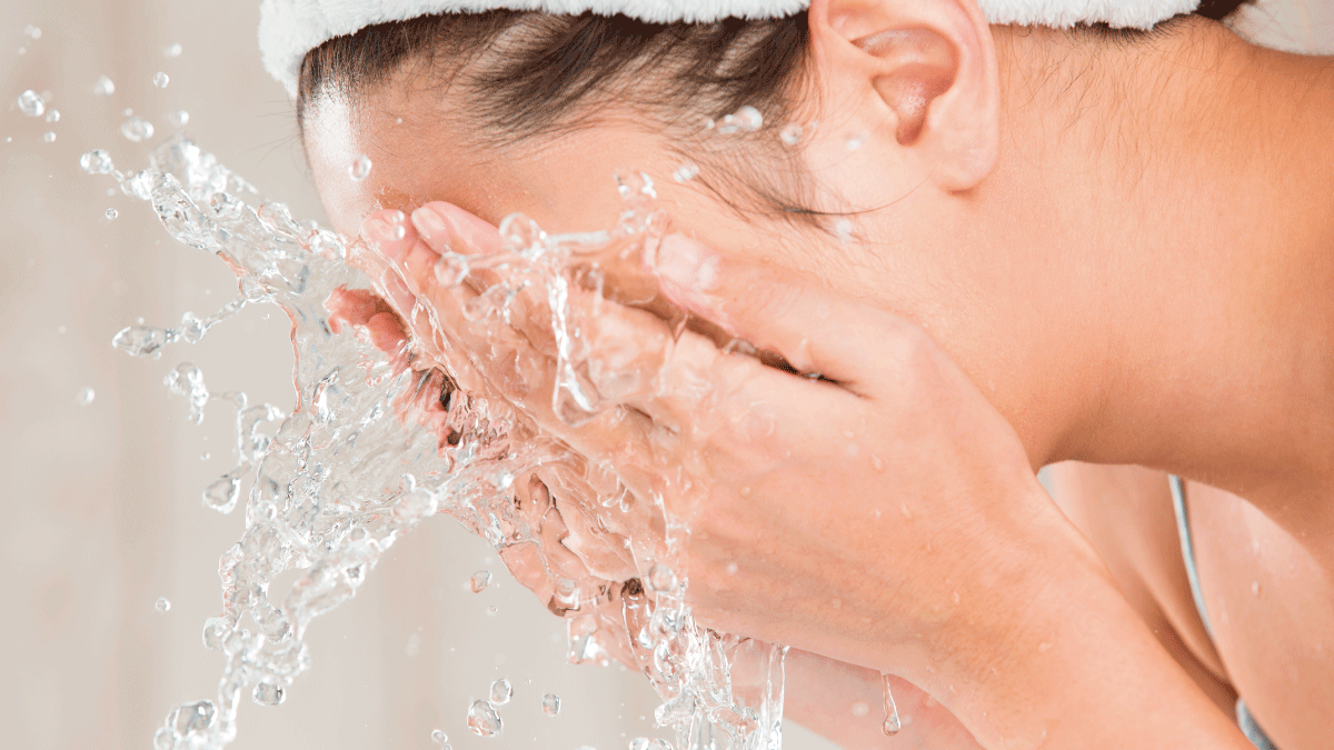 Primer plano de una persona lavándose la cara con agua a presión y una diadema blanca.
