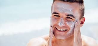 Un hombre sonriente se aplica protector solar en la cara en la playa.