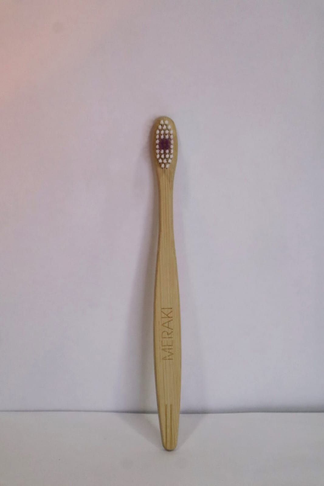 Cepillo de dientes de madera con cerdas moradas en posición vertical sobre un fondo blanco liso.