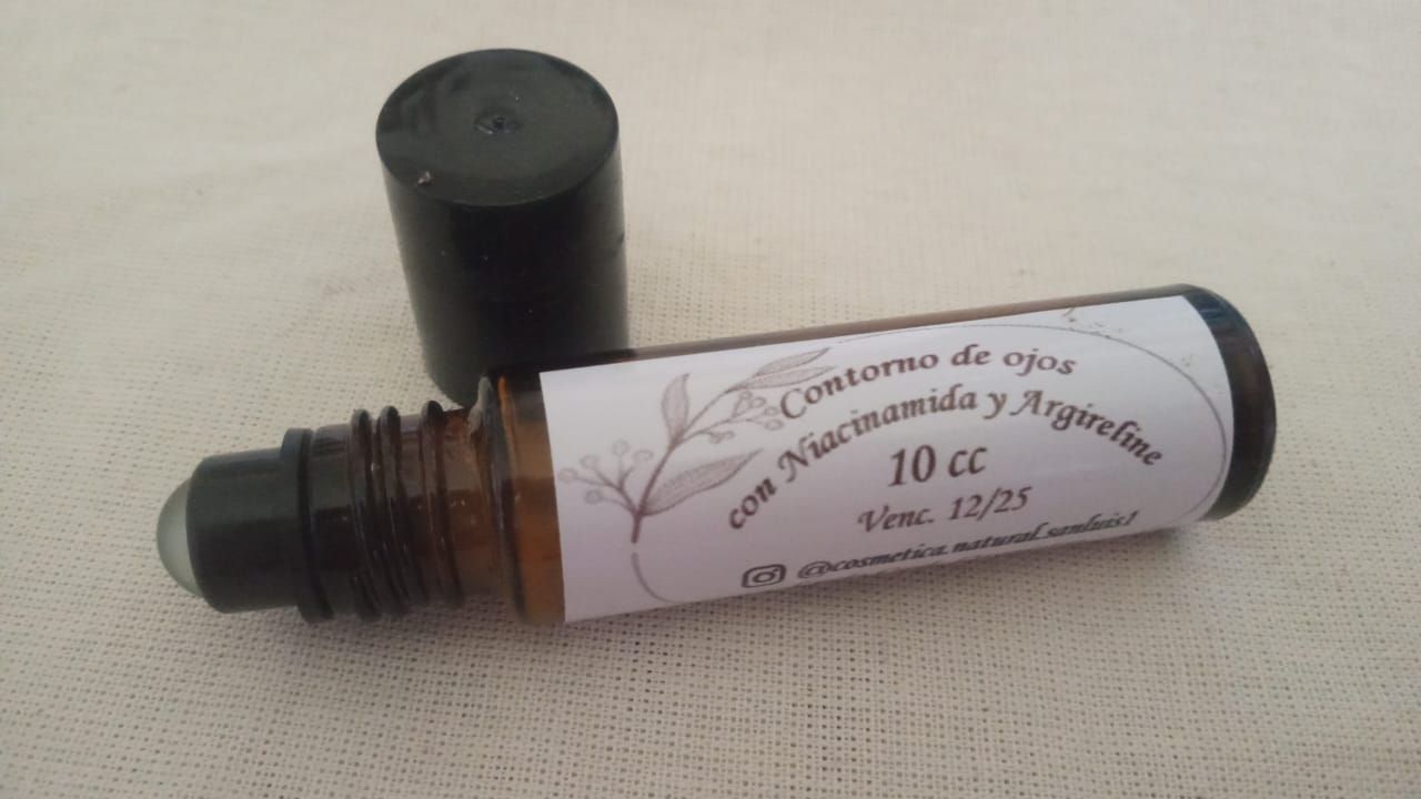 Frasco pequeño de cosméticos transparente con tapa negra, sobre una superficie clara junto a una tapa desprendida.
