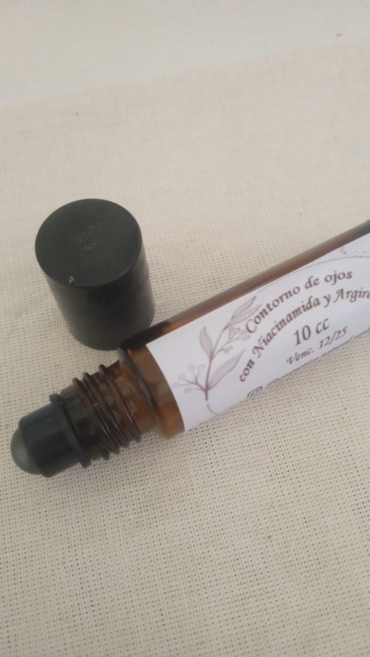 Frasco pequeño de cosméticos transparente con tapa negra, sobre una superficie clara junto a una tapa desprendida.