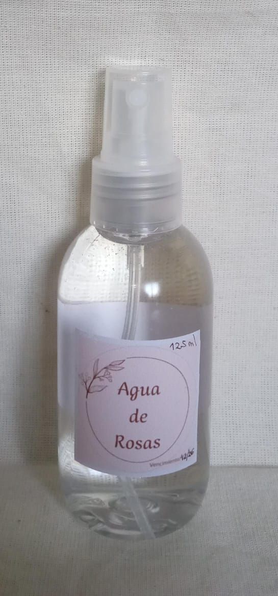 Botella de spray transparente con la etiqueta “Agua de Rosas” sobre un fondo de tela clara.