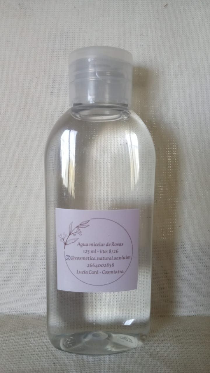 Botella de plástico transparente con tapón plateado y etiqueta rosa pálido sobre fondo de tela clara.