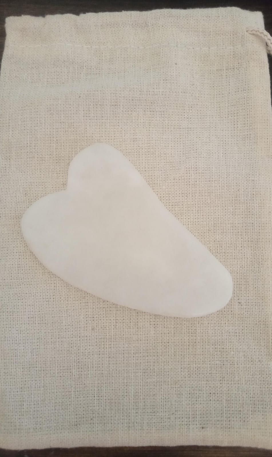 Objeto blanco con forma de corazón sobre un fondo de tela texturizada de color beige.