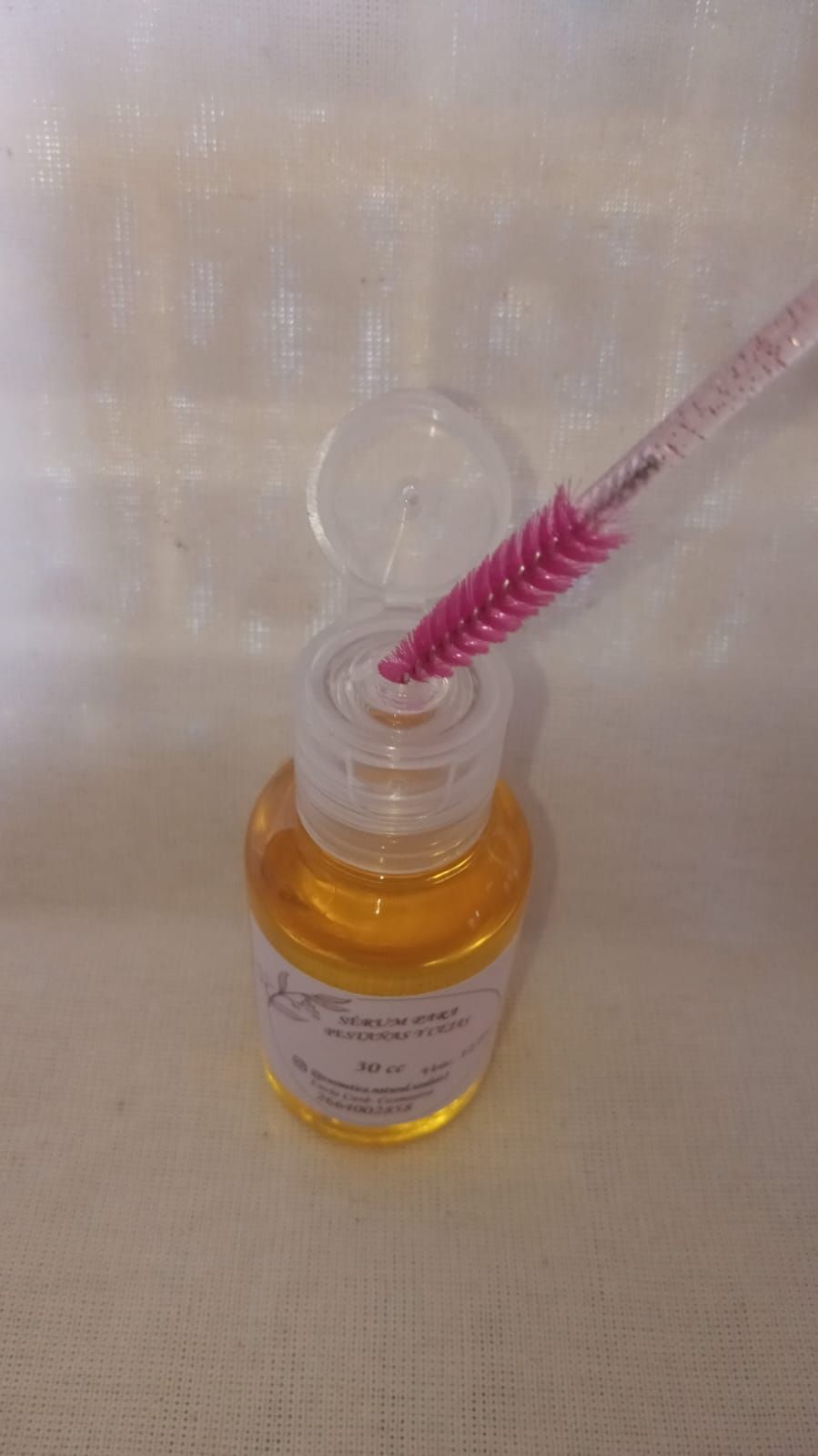Frasco de líquido color ámbar con tapón de pincel rosa y una pequeña etiqueta blanca.