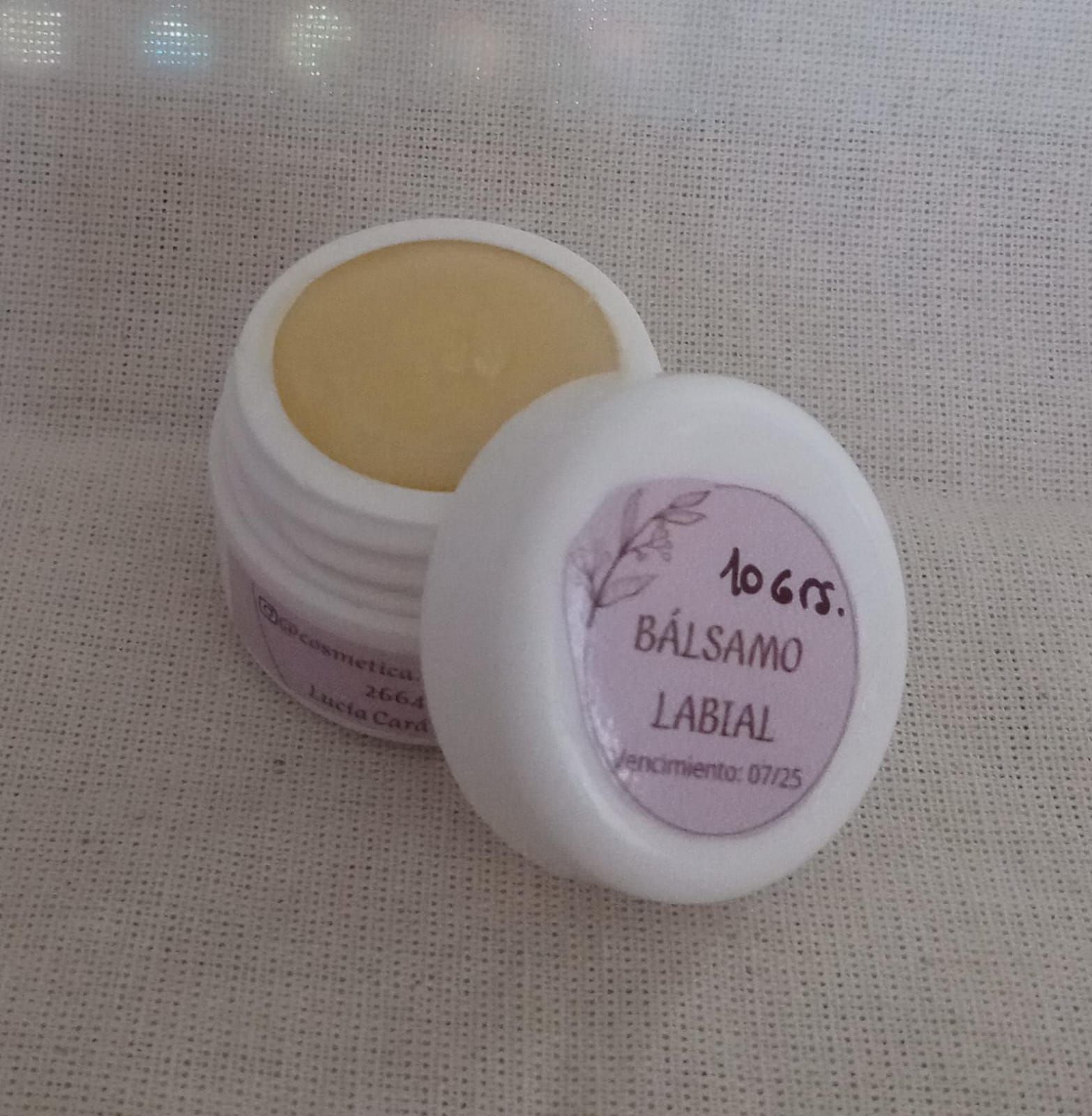 Dos pequeños frascos blancos de bálsamo labial, uno abierto con bálsamo beige y otro con la tapa etiquetada con la inscripción