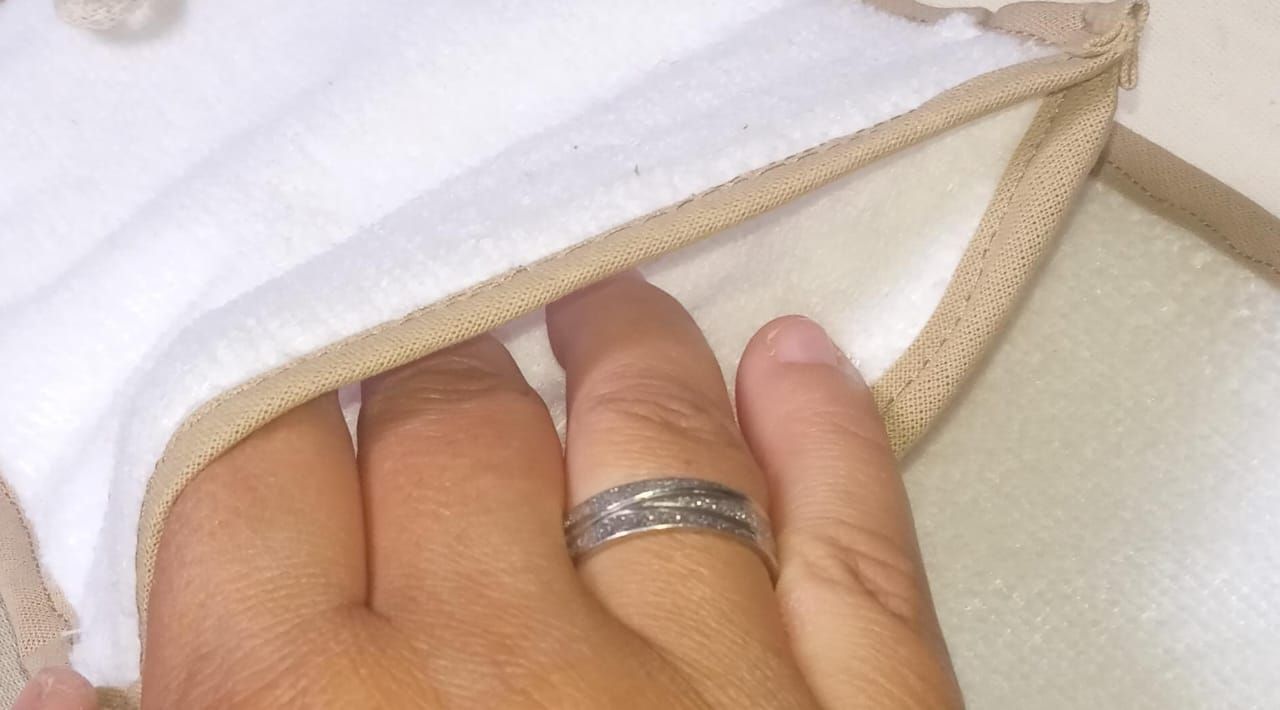 Esponja de baño beige con asa blanca para colgar sobre una superficie clara.