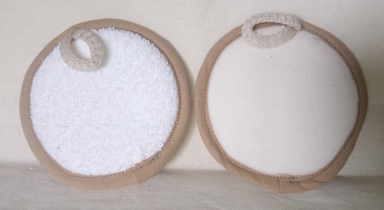 Dos almohadillas redondas de tela de rizo blanca con bordes beige y pequeñas presillas para colgar sobre una superficie clara.