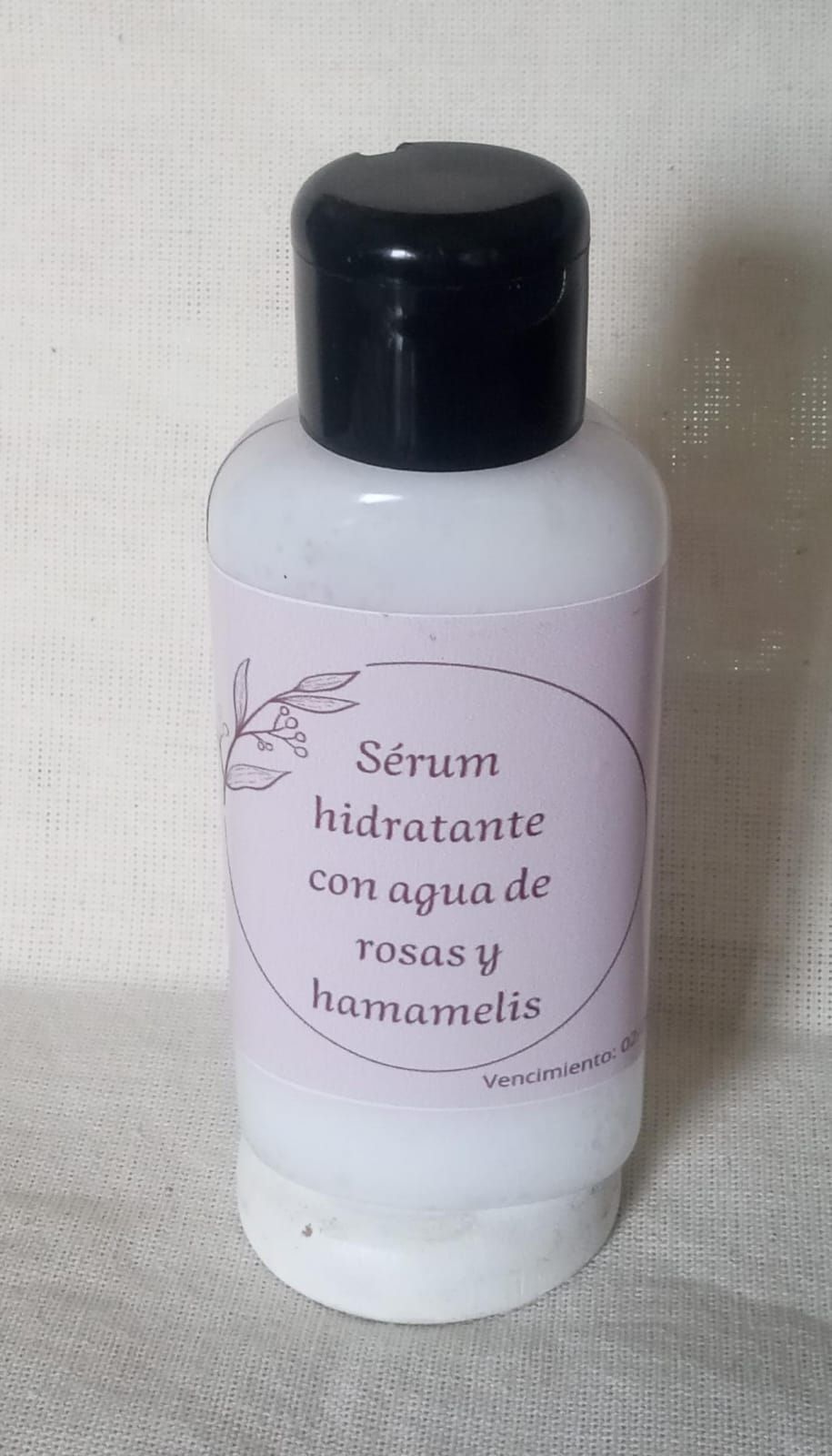 White bottle with black cap labeled “Serum hidratante con agua de rosas y hamamelis”