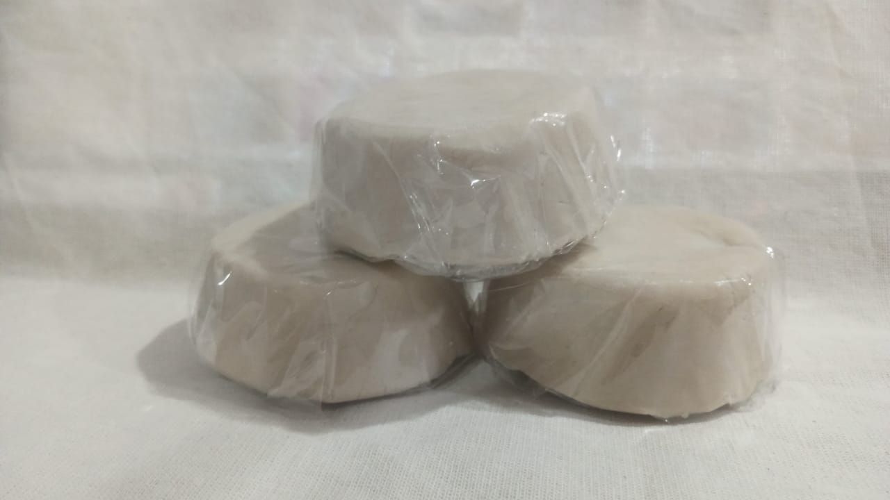 Tres tabletas redondas blancas envueltas apiladas sobre un fondo de tela blanca.