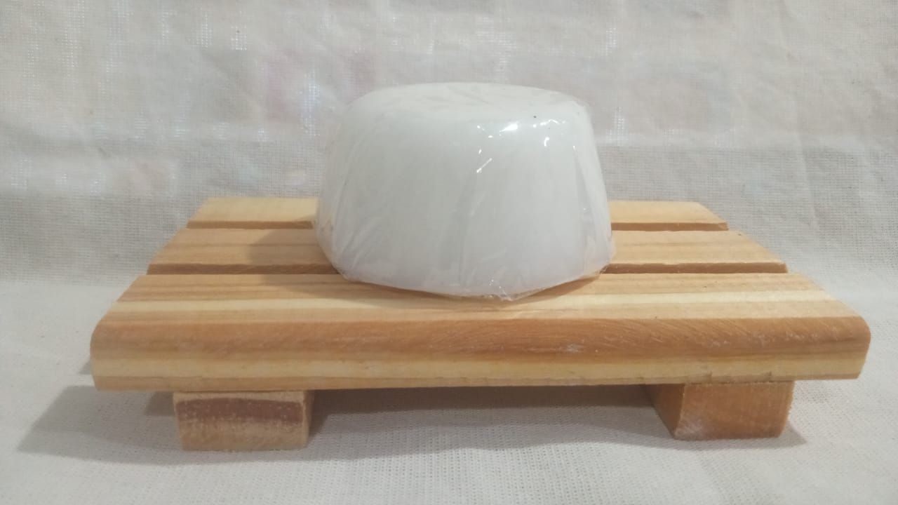 Objeto moldeado blanco sobre una pequeña plataforma de madera a rayas sobre un fondo de tela clara.
