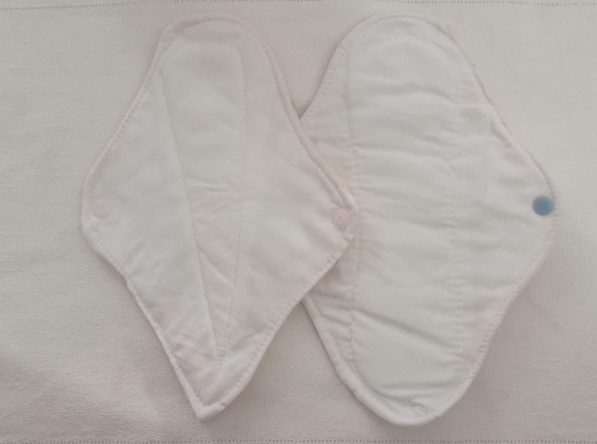 Dos compresas menstruales de tela blanca con cierres de broche azules colocadas una al lado de la otra.