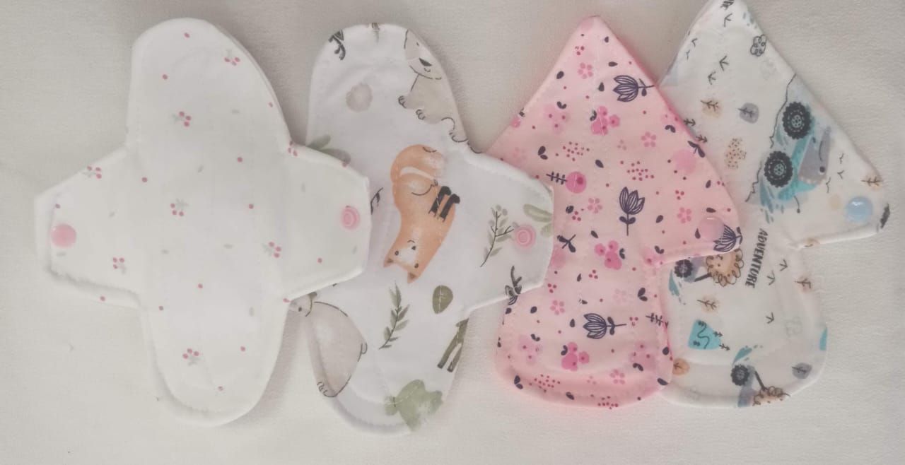 Almohadillas de tela surtidas con estampados florales y de animales en tonos pastel, dispuestas sobre una superficie blanca.