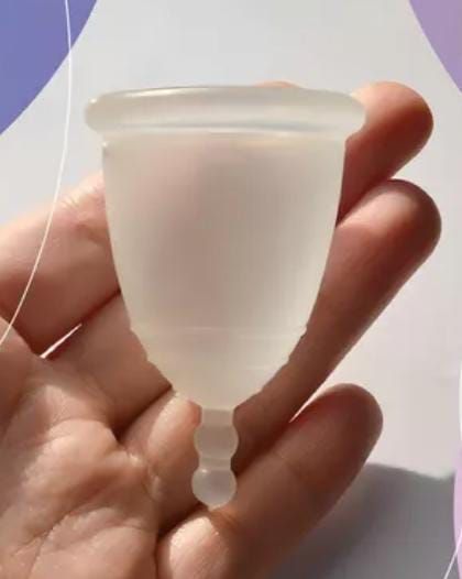 Una mano sosteniendo una copa menstrual de silicona translúcida con un tallo corto.