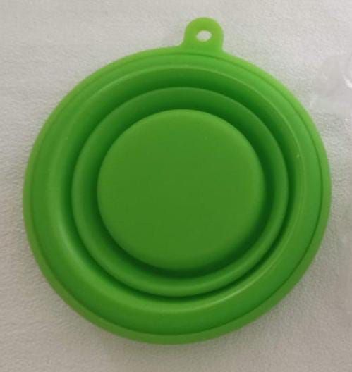 Bol plegable de silicona verde con una pequeña argolla para colgar, mostrado sobre un fondo blanco.