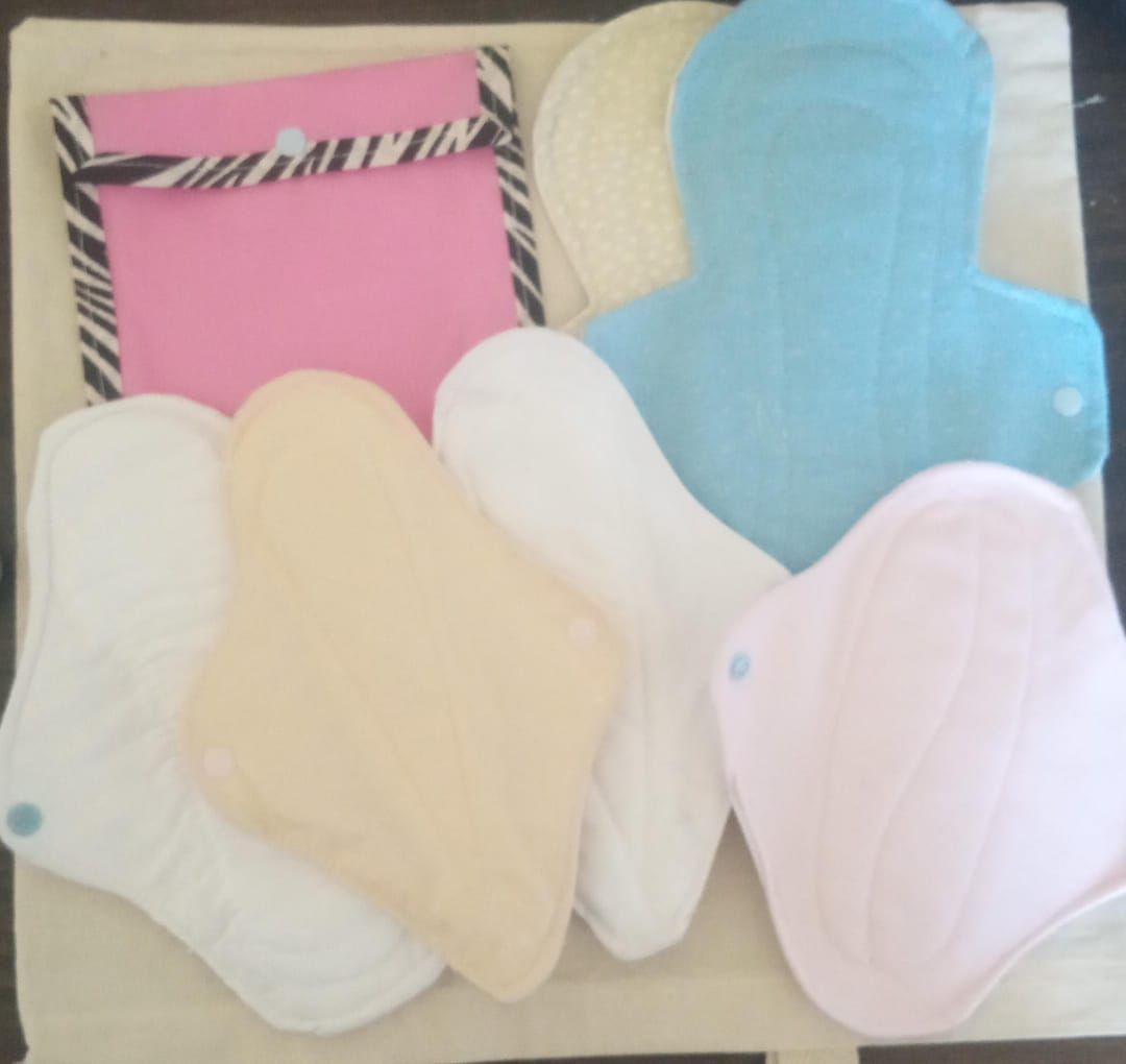 Compresas de tela reutilizables de varios colores: rosa, azul, beige y blanco, sobre una mesa.