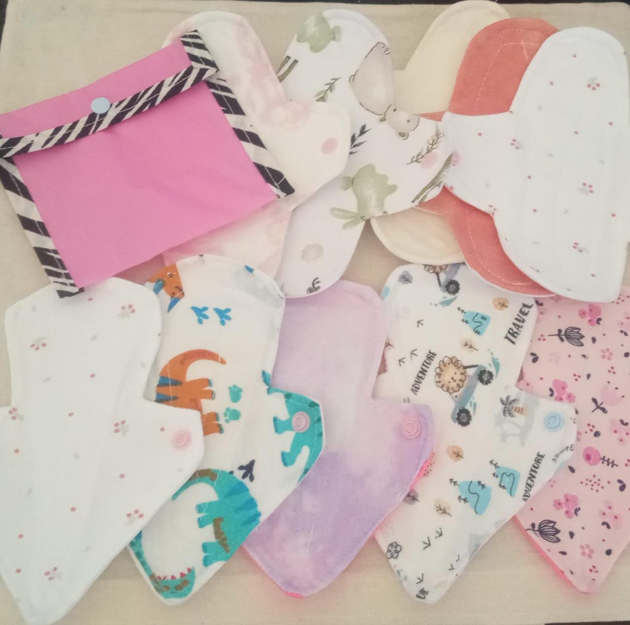 Surtido de compresas y protectores de tela reutilizables de colores con estampados de corazones, flores y diseños divertidos sobre un fondo claro.
