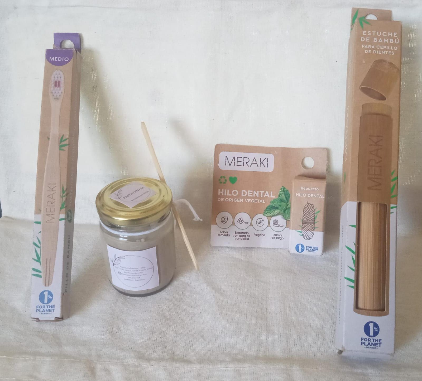 Artículos variados empaquetados sobre una tela blanca, que incluyen dos cajas largas, un frasco y una bolsita pequeña con una cuchara.