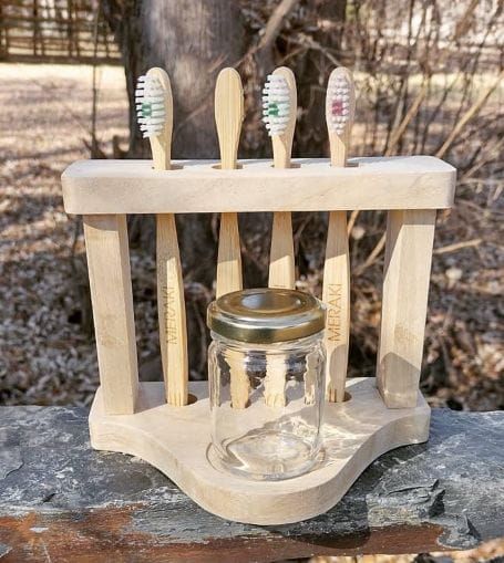 Soporte de madera para cepillos de dientes con cuatro cepillos y un frasco transparente sobre una superficie de piedra al aire libre.