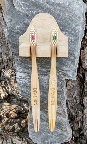 Dos cepillos de dientes de bambú colgados de un pequeño soporte de madera contra una pared de roca.