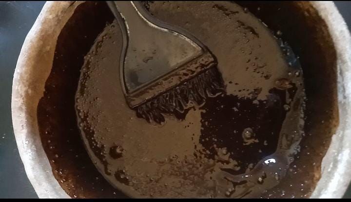 Revolviendo con una cuchara la salsa marrón oscura en un tazón o cacerola de metal, con residuos alrededor de los bordes.