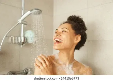 Una persona se ducha y sonríe bajo el agua corriente en un baño alicatado.