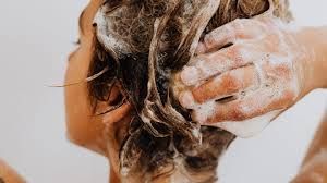 El cabello se está lavando con champú, mostrando una mano que masajea la espuma en los rizos mojados.