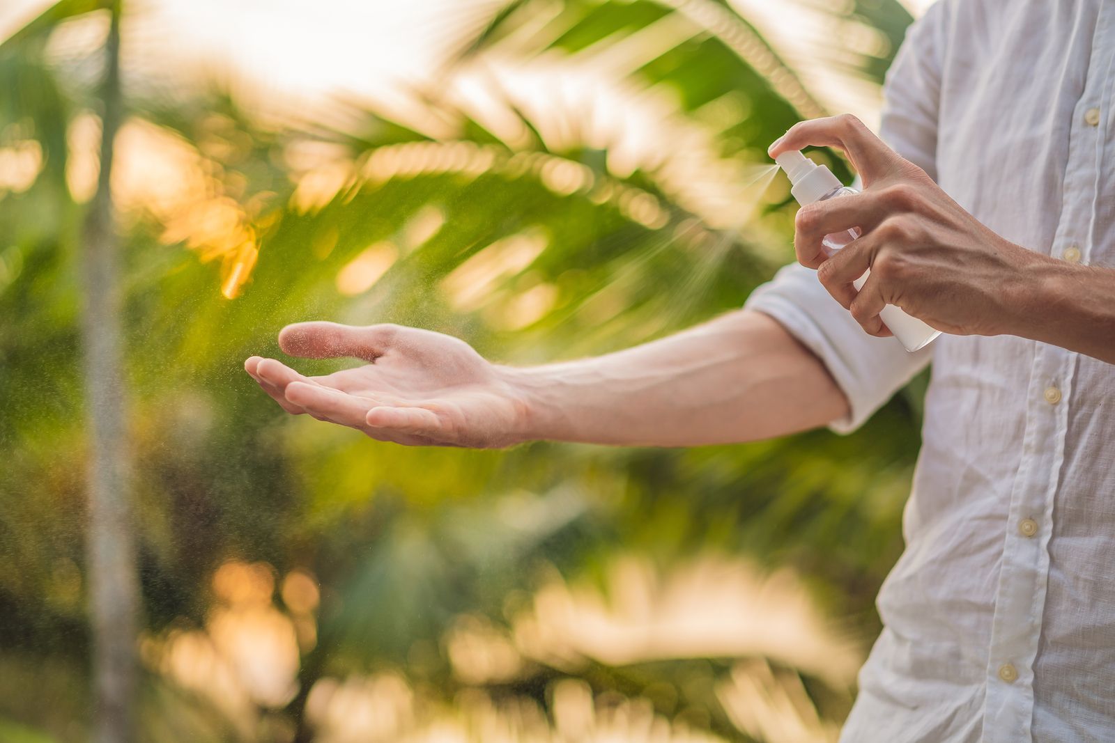 Una persona se aplica protector solar en el brazo extendido al aire libre, con vegetación tropical de fondo.