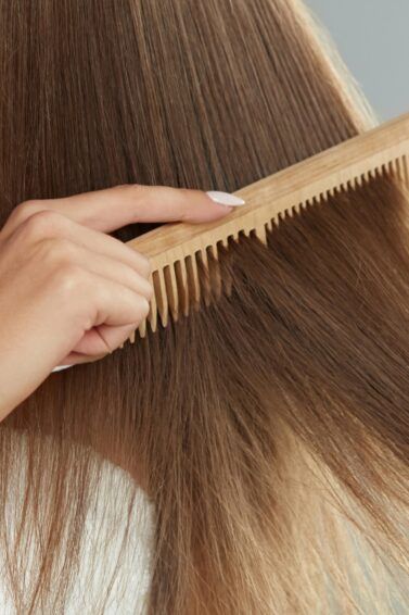 Peinar a mano el cabello largo, liso y castaño claro con un peine de madera.