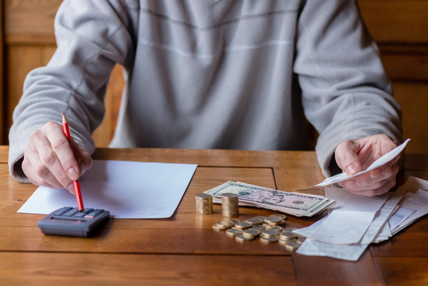 Person calculating finances at a table with money, calculator, receipts, and a pencil.
