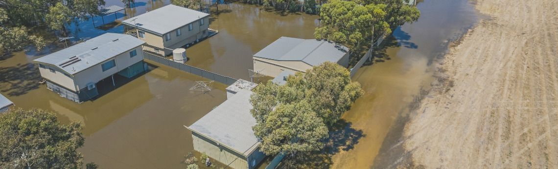 Houses surrounded by floodwaters. Aerial view shows elevated structures, trees, and flooded farmland.