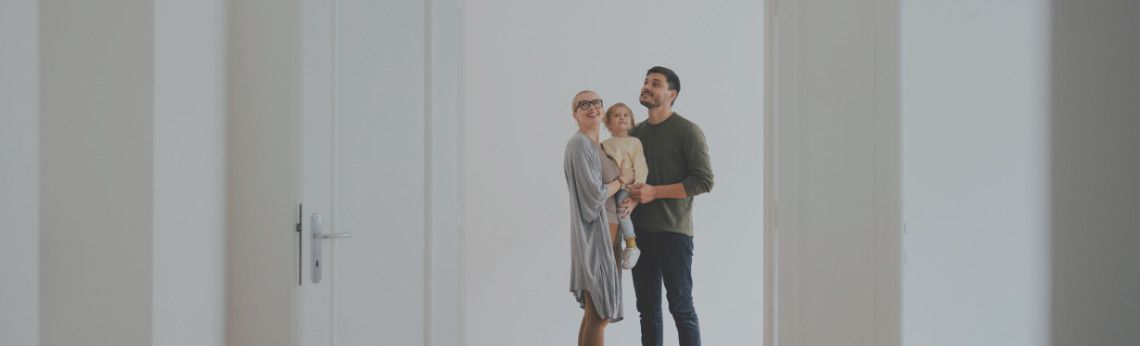 A family of three, standing in an empty white room, looking up.