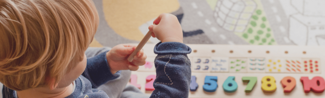 A child using a pencil to touch colorful numbers on a learning board.
