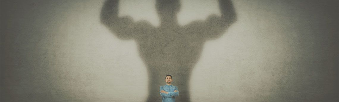 A small figure stands under the shadow of a large, muscular figure with raised arms.